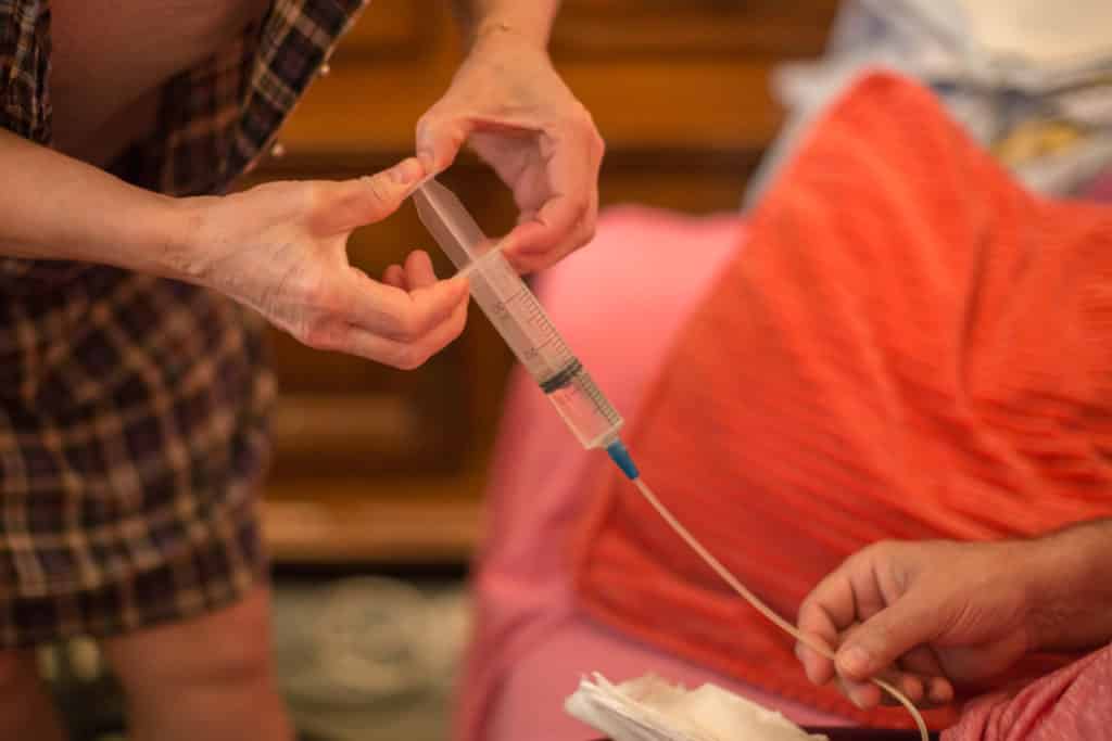 Les infirmiers de l’HAD ont appris à l’épouse du patient à se servir de la pompe d’alimentation entérale. C’est donc elle qui nettoie la sonde (photo ci-dessus) avant de connecter les tubulures pour l’alimentation de son mari. Avant de lancer « la machine », Elodie vérifie que toutes les connexions ont été correctement effectuées. © Pascal Vo