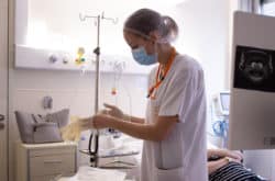 Une IRC infirmière de recherche clinique de l'unité d'investigation de l'Institut Curie réalise un soin dans la chambre d'une patiente atteinte d'un cancer et incluse dans un protocole